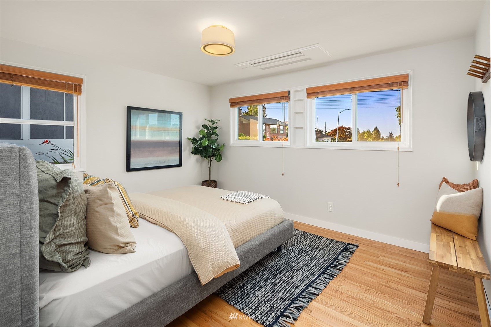 Furnished bedroom with a gray bed, hardwood floors, and wide windows overlooking the neighborhood.
