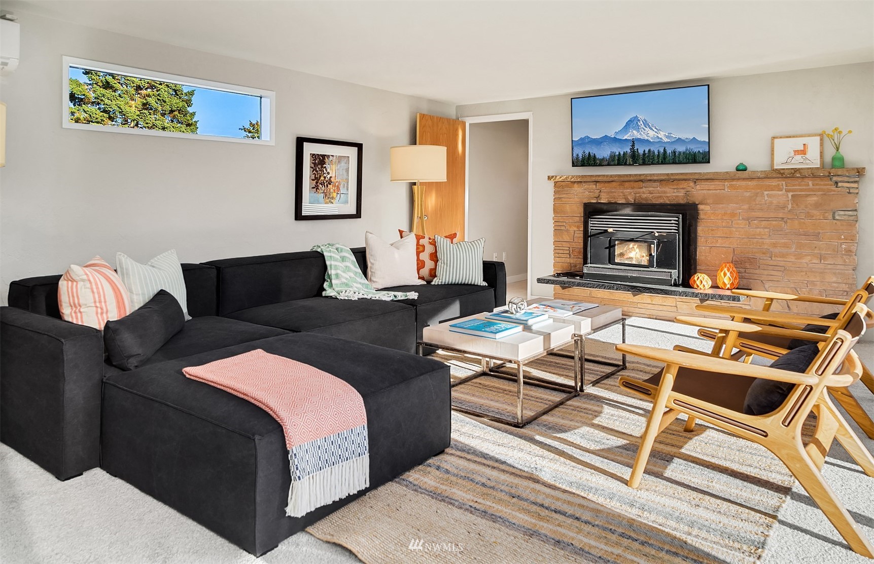Staged living room with a black sectional, wood lounge chairs, and a stone fireplace.