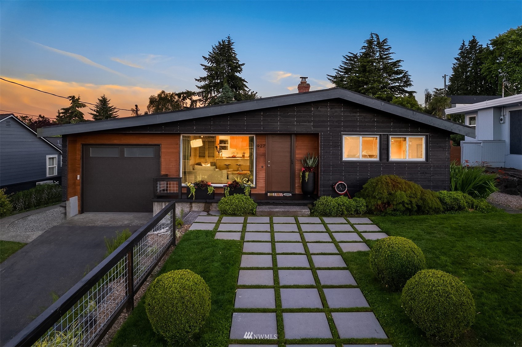 Single-story home with dark siding, wood accents, and a paver walkway at dusk.