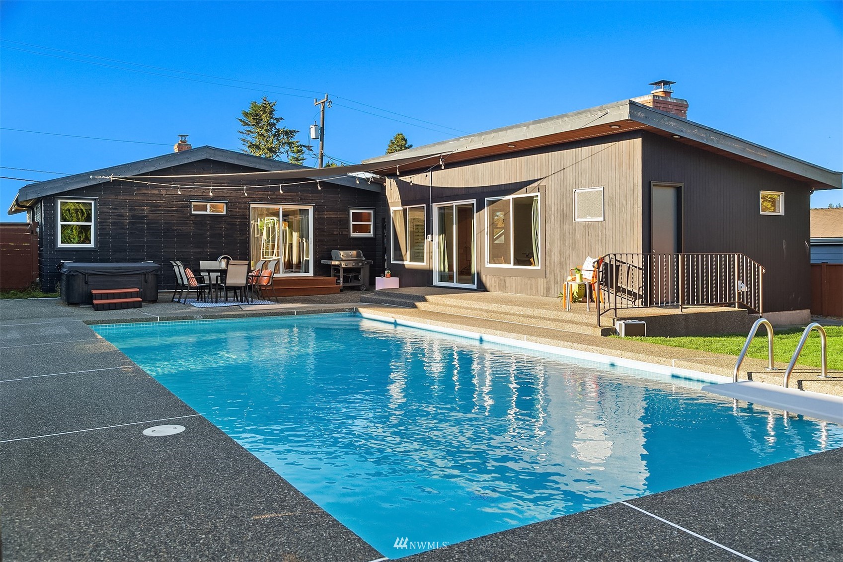 Back of a single-story home beside a swimming pool, hot tub, and furnished patio.