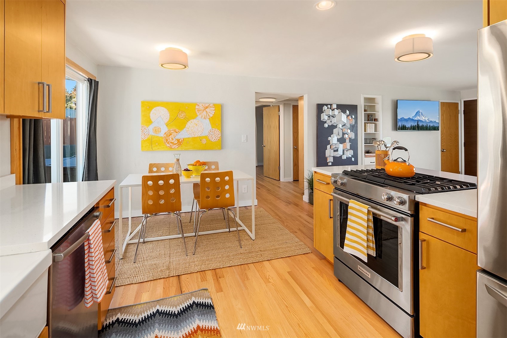 Kitchen with honey-colored cabinets, hardwood floors, and a stainless steel range beside a dining table.