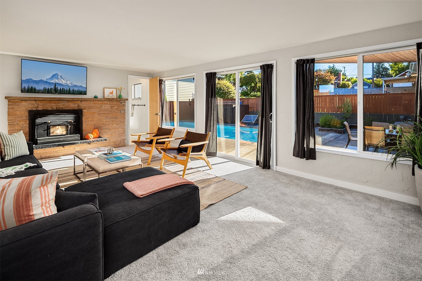 Living room with a stone fireplace, dark sectional, and windows overlooking an outdoor pool.