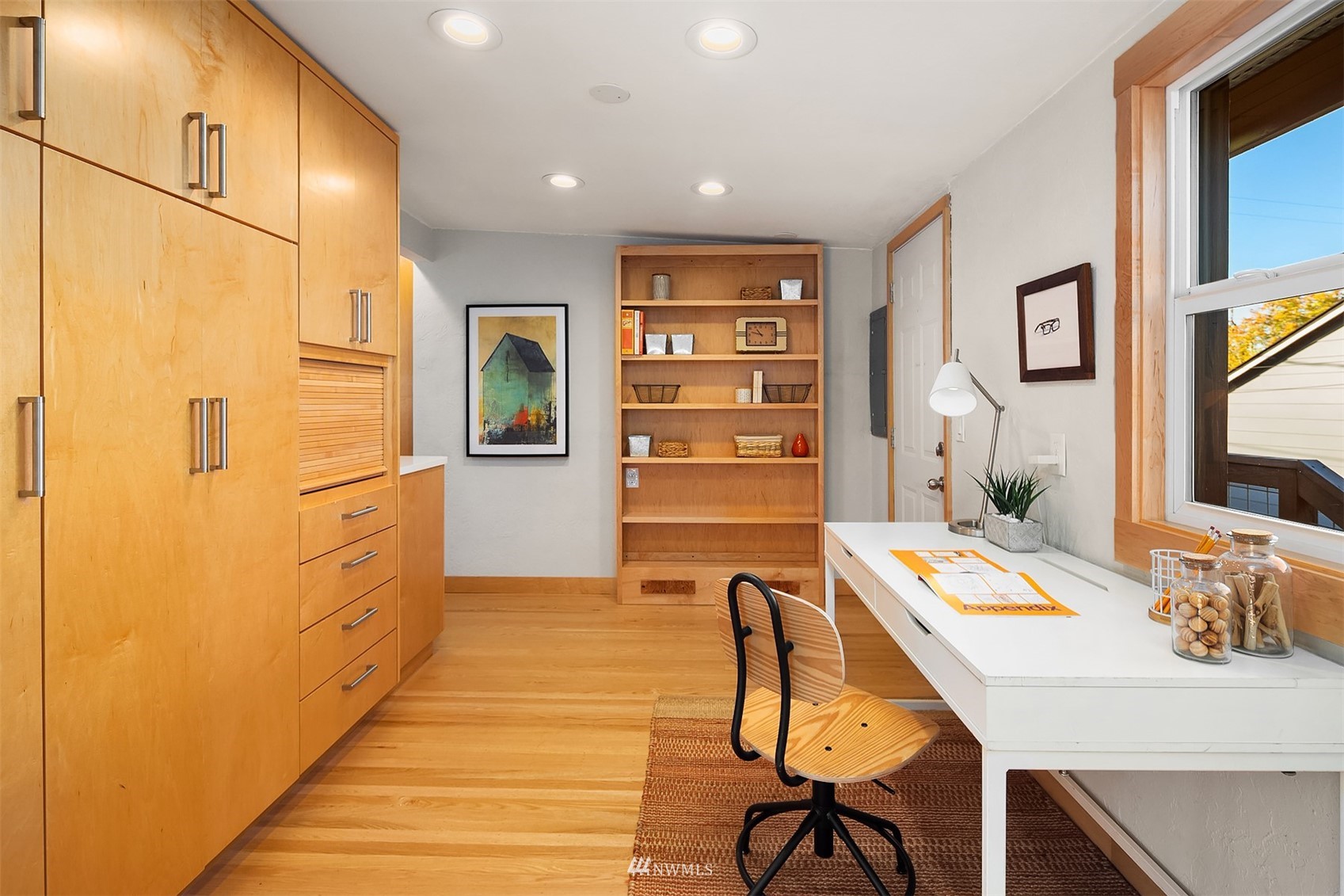 Home office with honey-colored built-ins, a white desk, and a large wood-trimmed window.
