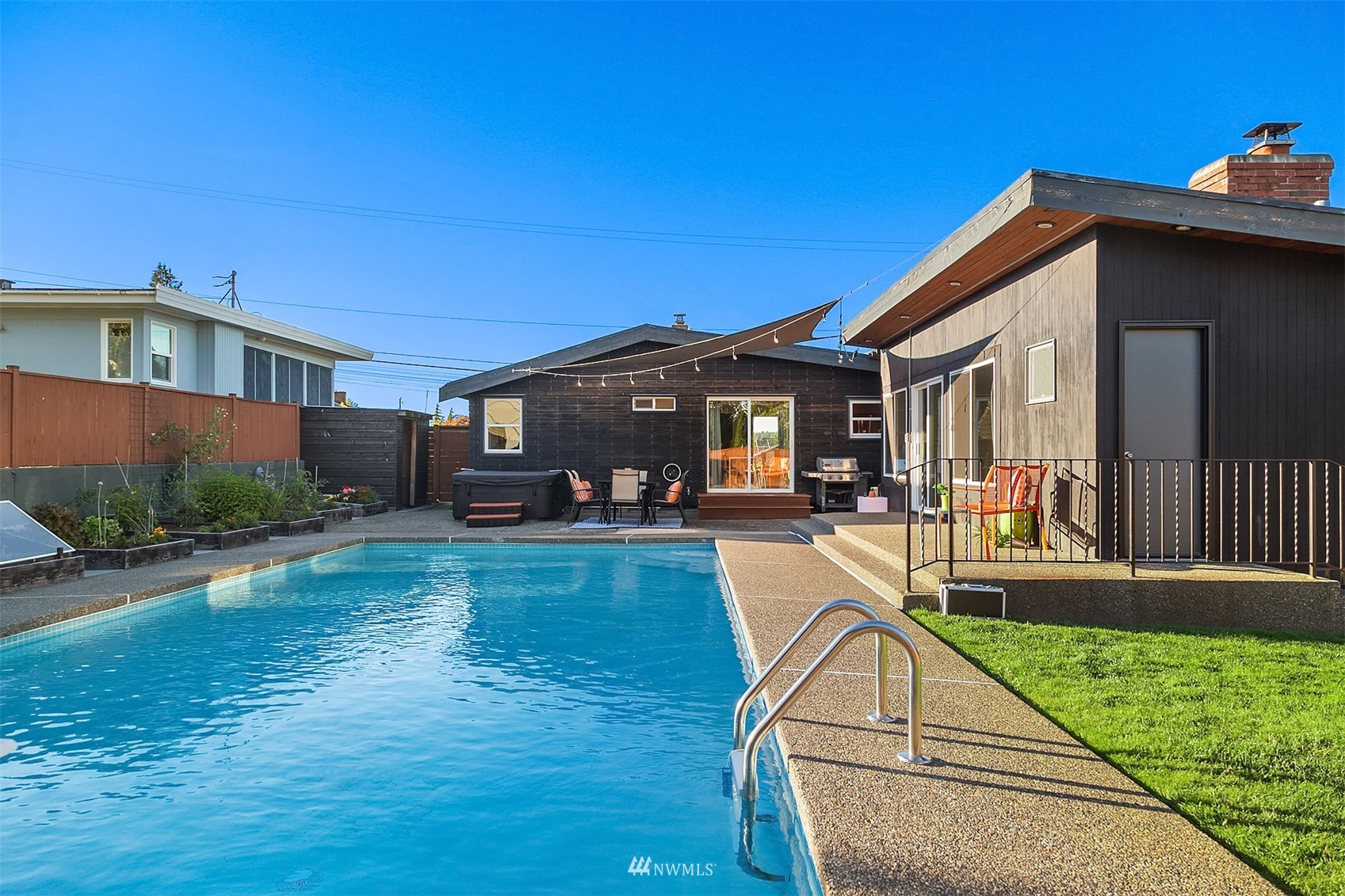 Backyard swimming pool beside a modern home, with patio seating and a hot tub.
