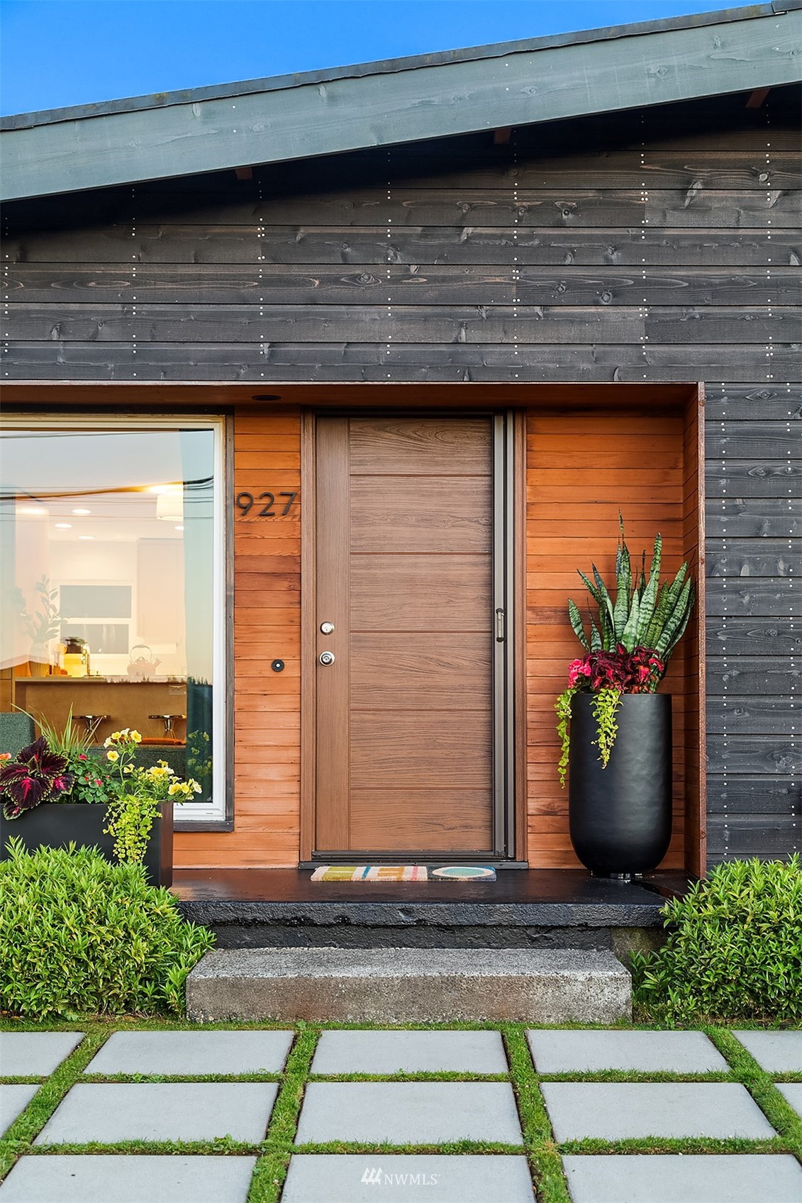 Home entrance with a horizontal wood door, cedar siding, potted plants, and a stepping-stone path.