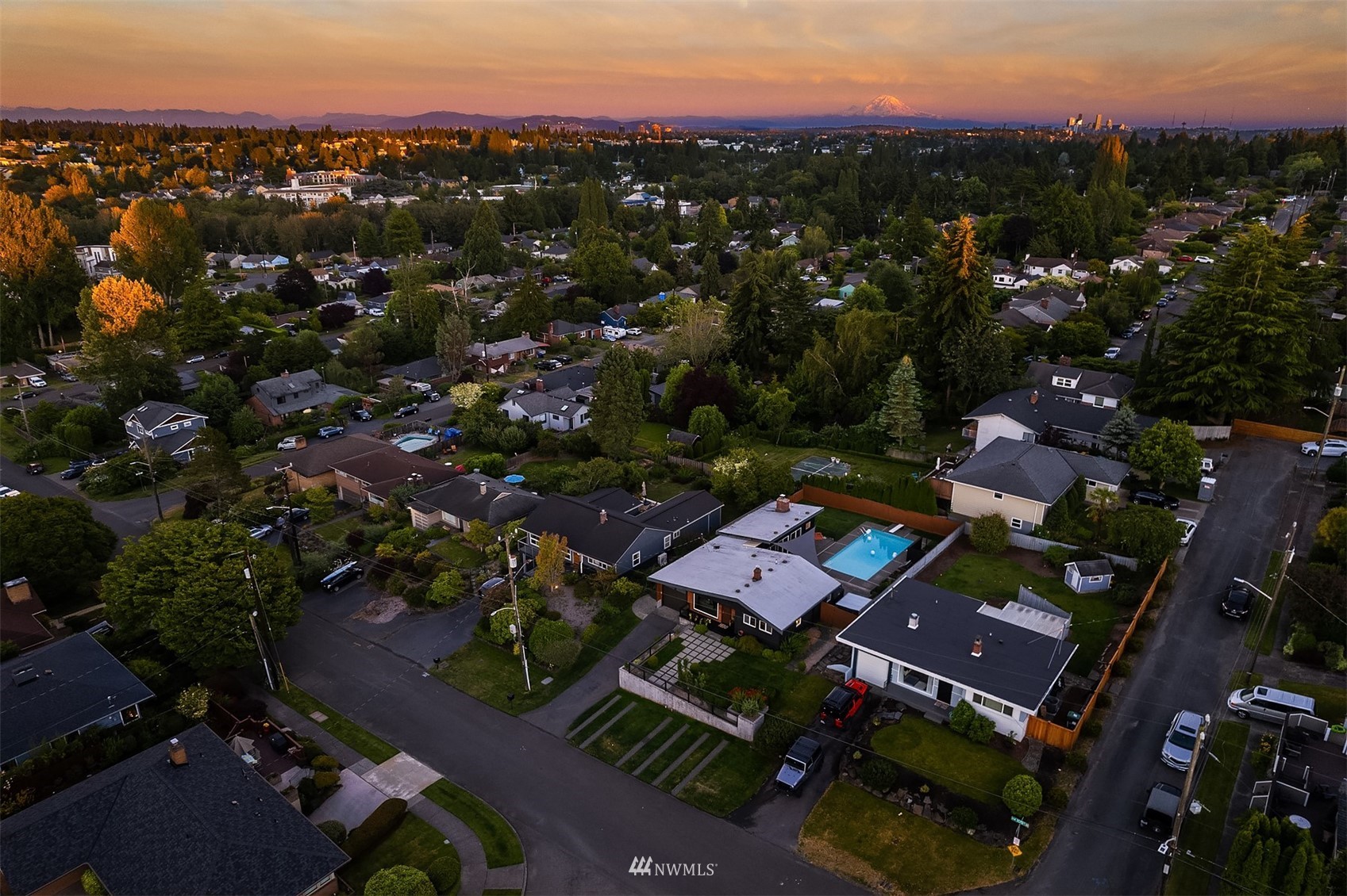 Aerial view of a Seattle neighborhood at sunset, with a backyard pool and snow-capped mountain in the distance.