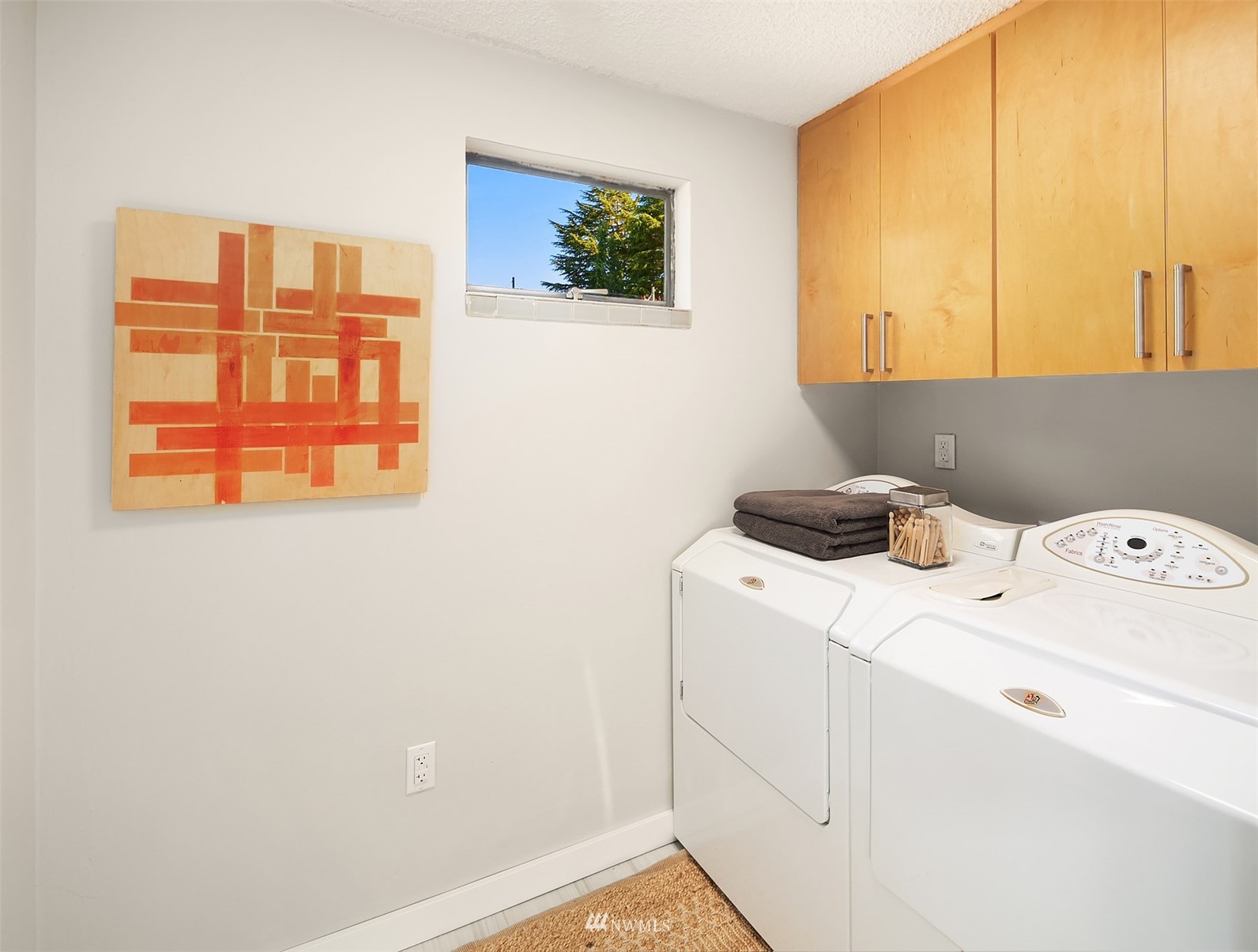 Laundry room with washer and dryer beneath light wood cabinets and a small high window.