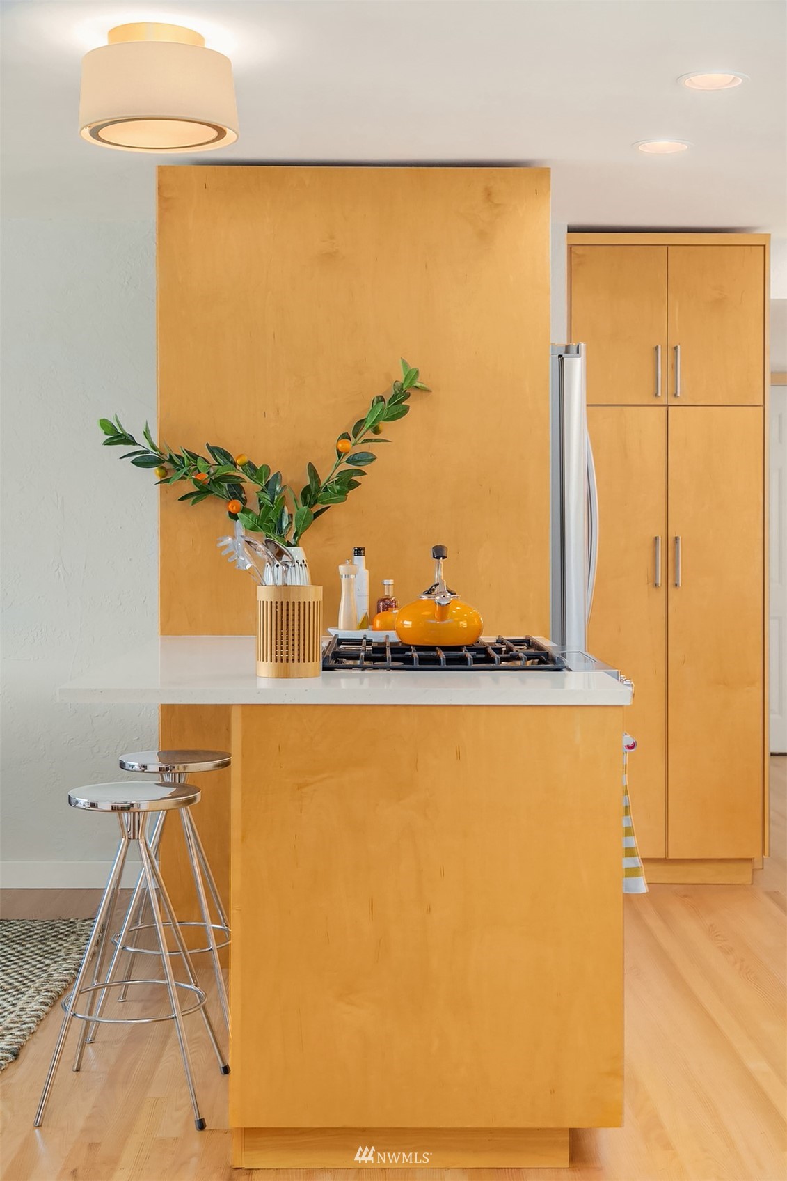 Modern kitchen with a honey-colored wood island, gas cooktop, and chrome bar stools.