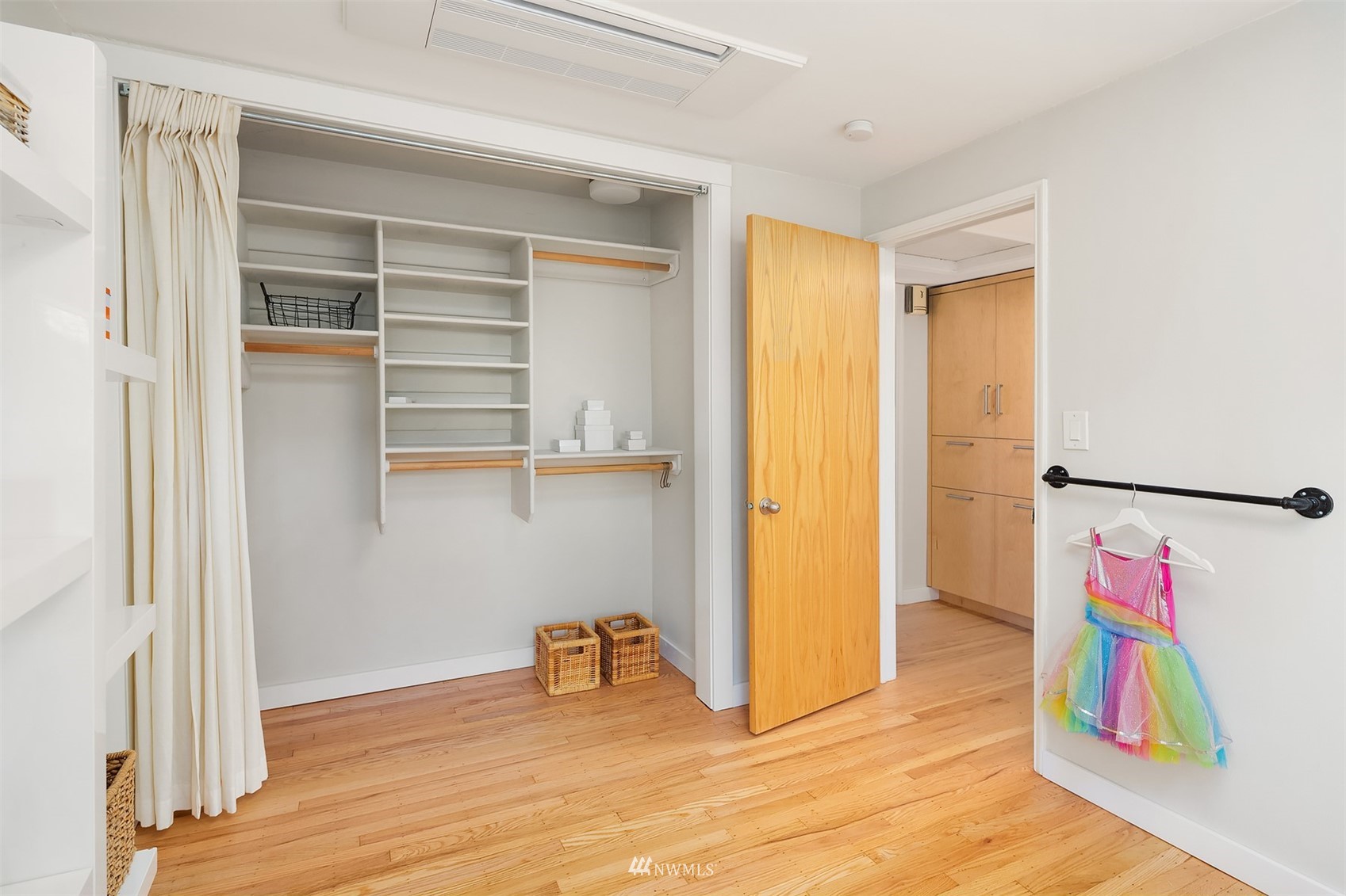 Walk-in closet with built-in shelving, a white curtain, and a colorful child’s dress hanging by the doorway.