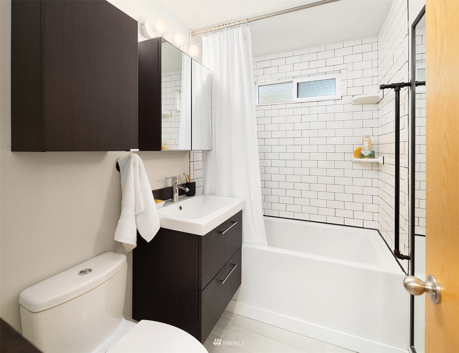 Bathroom with a white subway-tile tub surround, frosted window, and dark wood vanity.