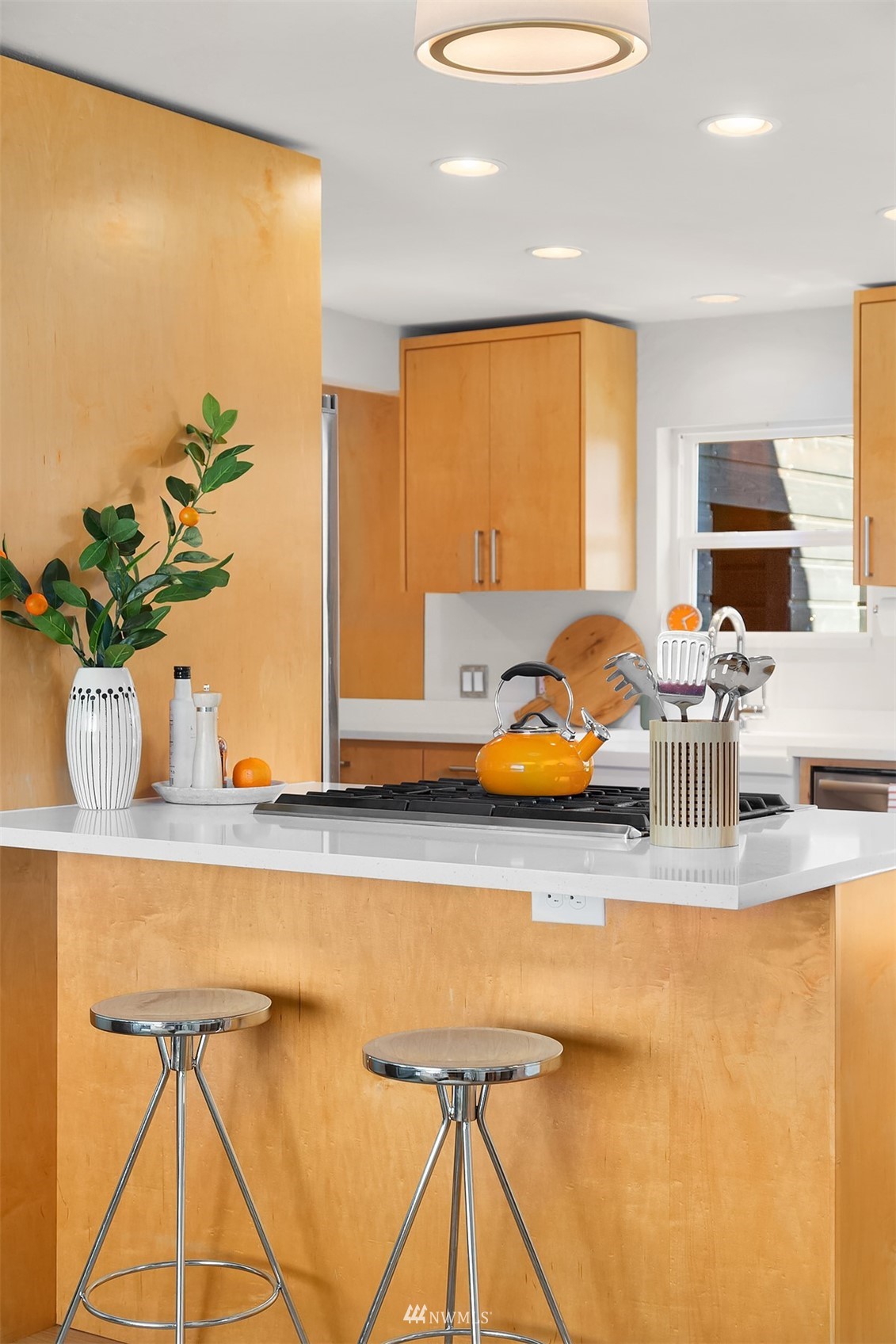 Kitchen with warm maple cabinets, a white island, gas cooktop, and two chrome stools.