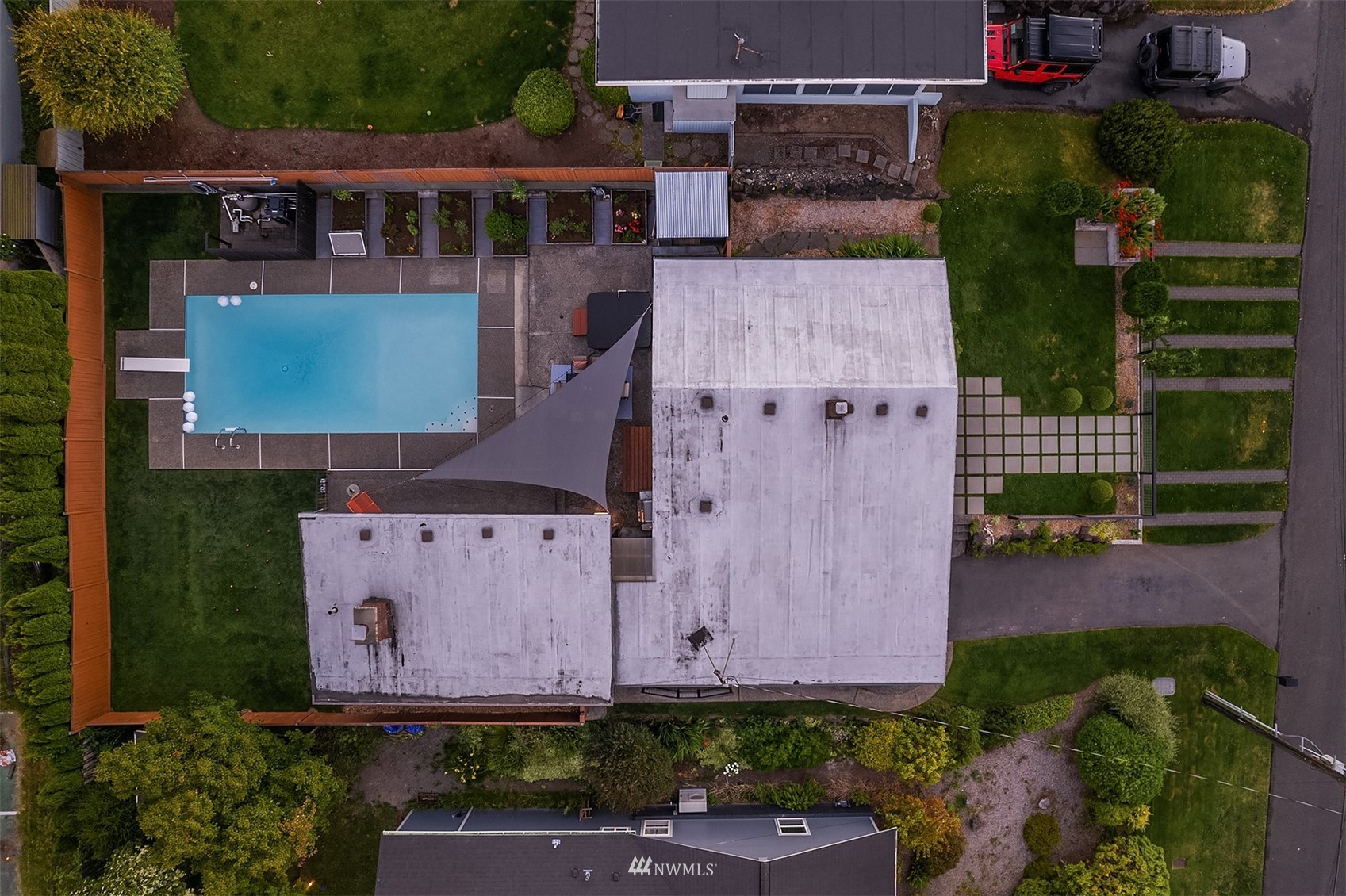 Aerial view of a home with a rectangular pool, patio, raised garden beds, and landscaped lawn.