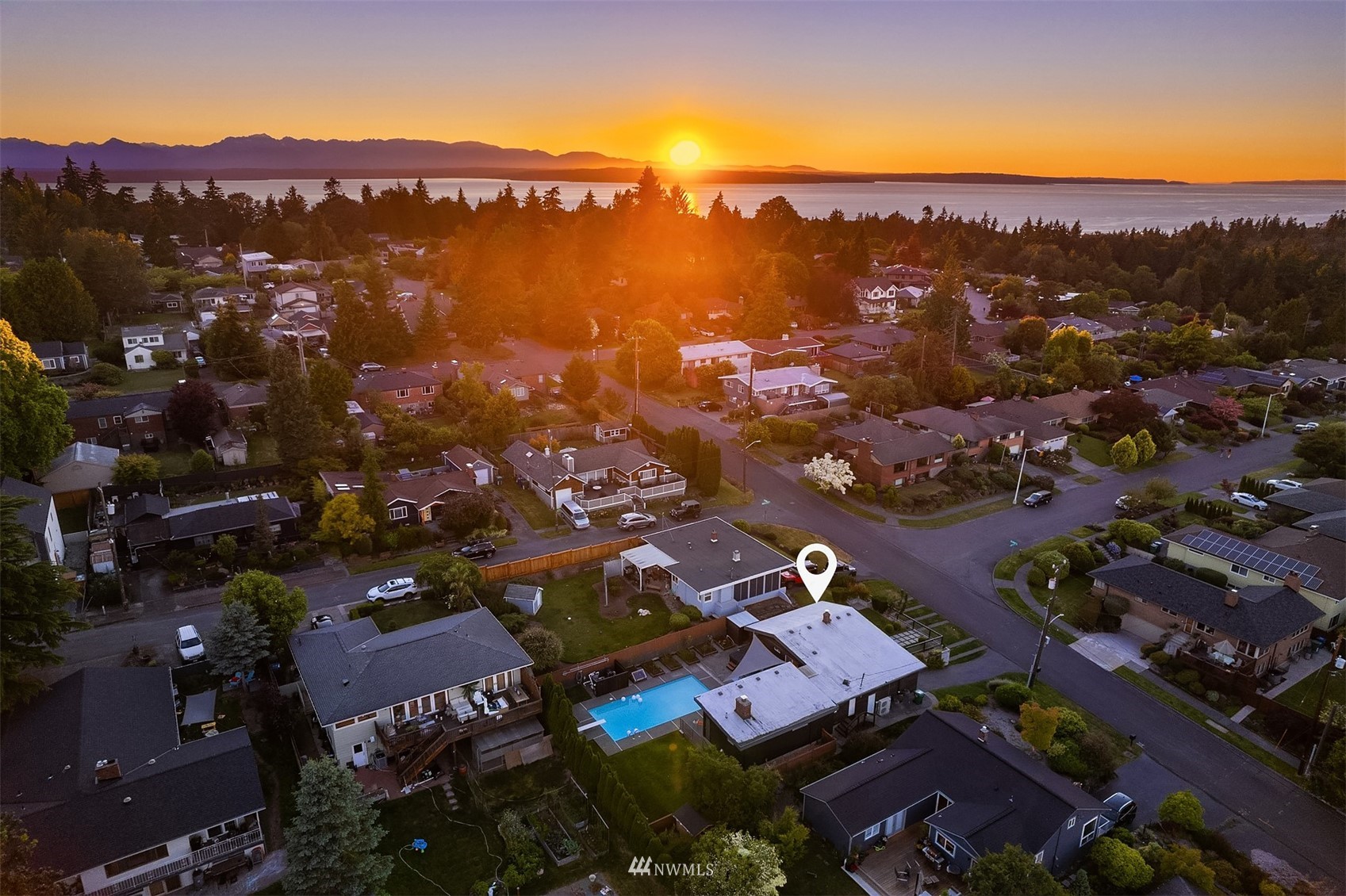 Aerial neighborhood view at sunset, with Puget Sound and mountain silhouettes beyond.