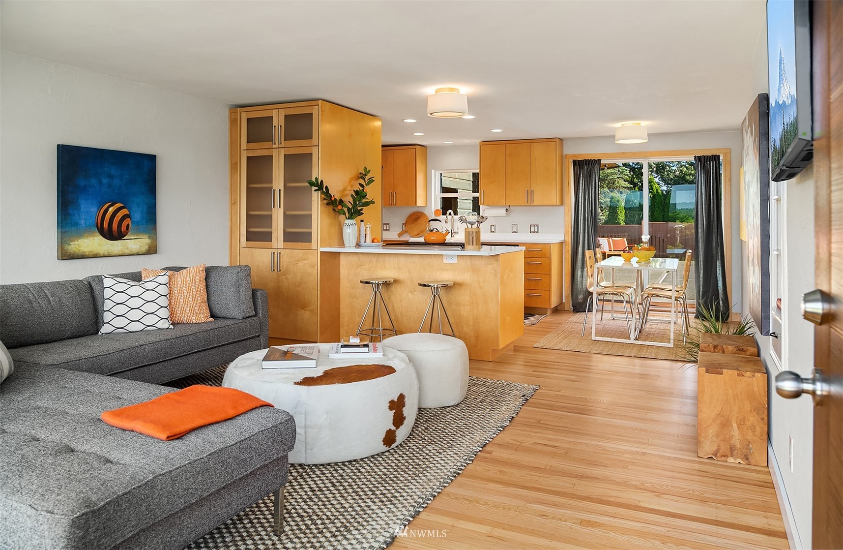 Open-plan living room and kitchen with a gray sectional, wood cabinetry, and sliding doors to a deck.
