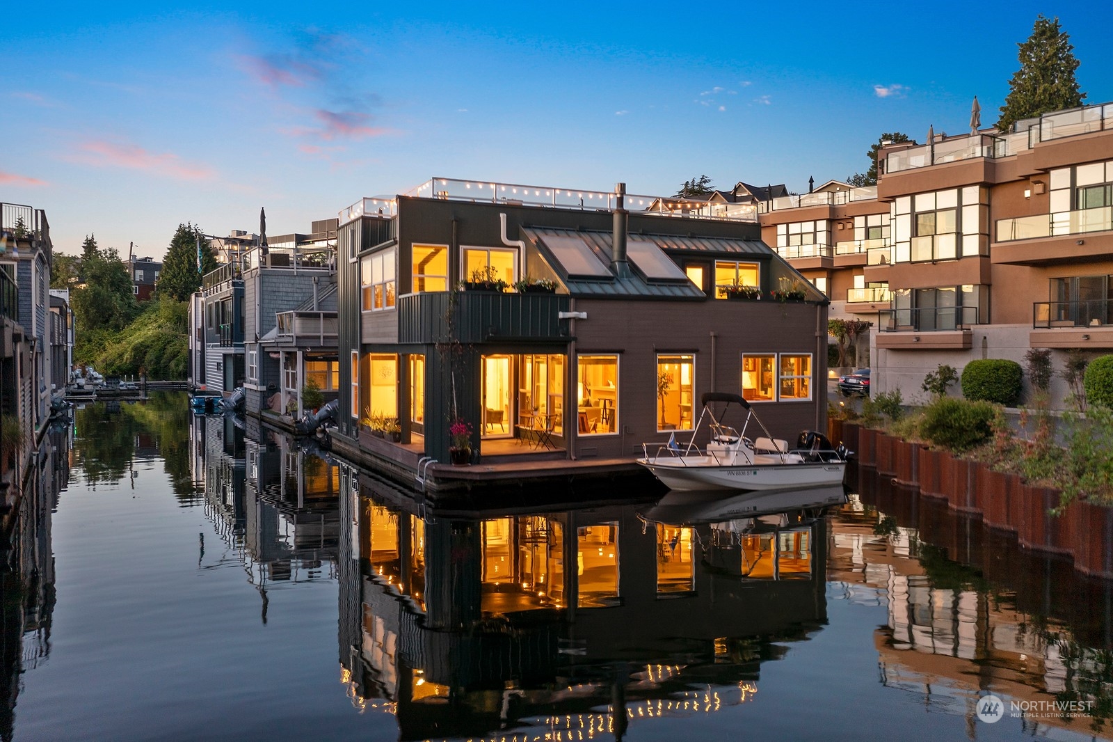 Canal-side home glowing at dusk, with a boat moored alongside and lights reflected in the water.