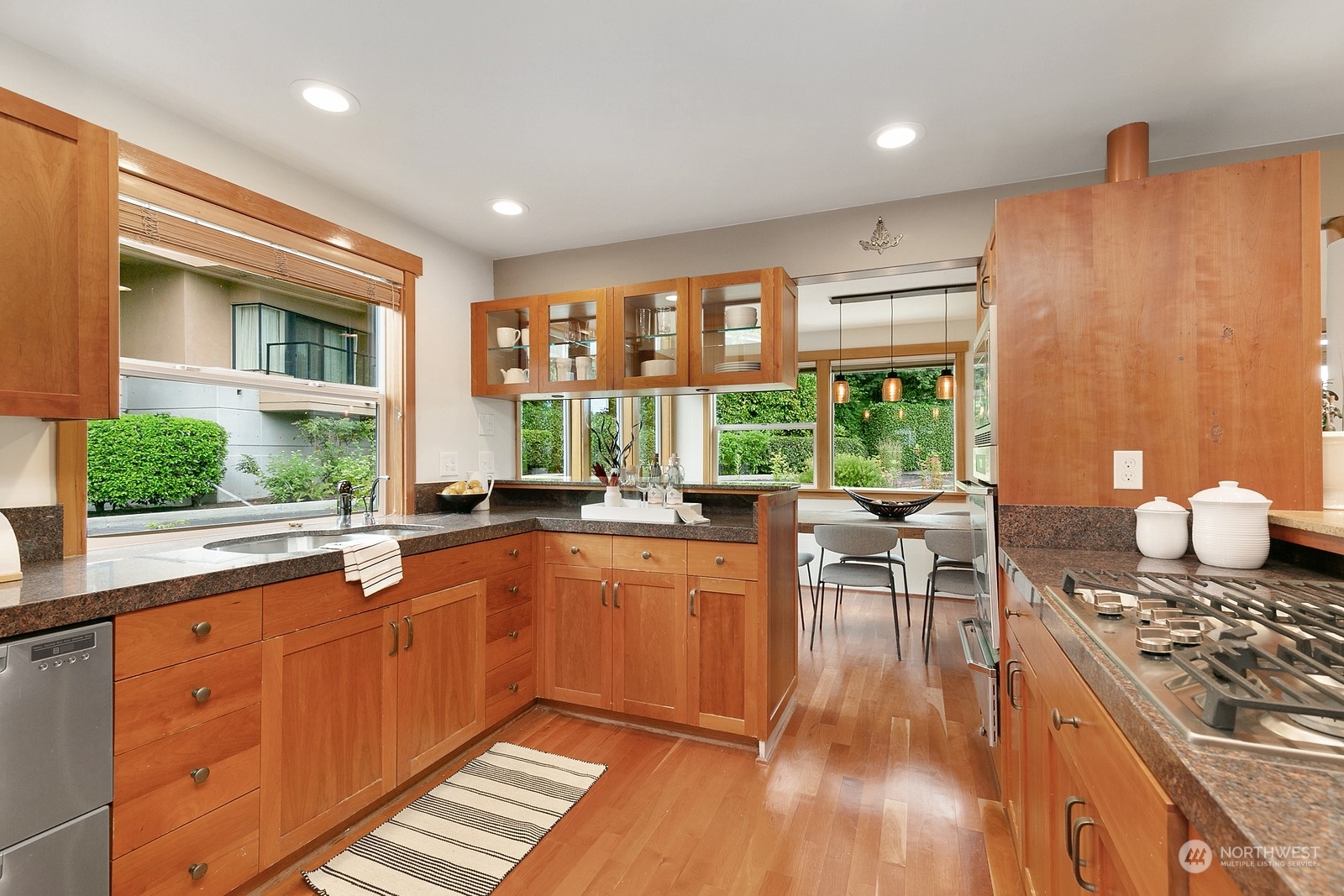Kitchen with warm wood cabinets and granite counters, opening to a dining area beside garden-facing windows.