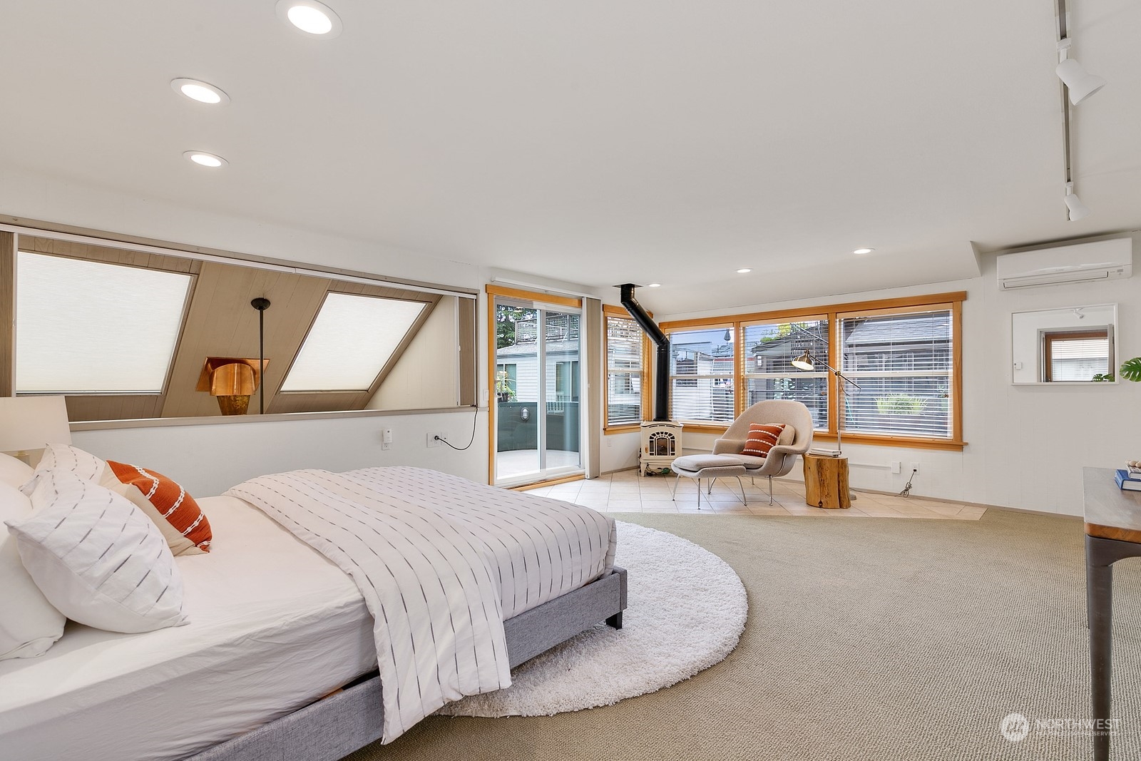 Bedroom with angled ceiling windows, a sitting area, and broad wood-framed windows.