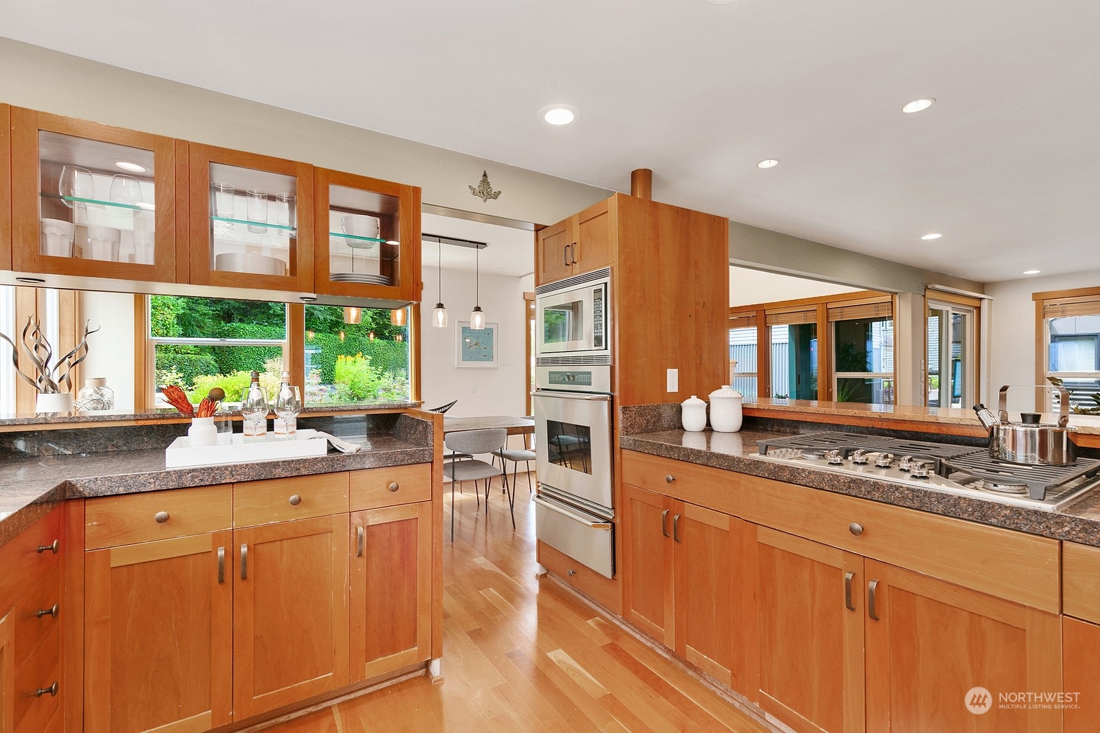 Kitchen with warm wood cabinetry, granite counters, stainless appliances, and windows overlooking a garden.