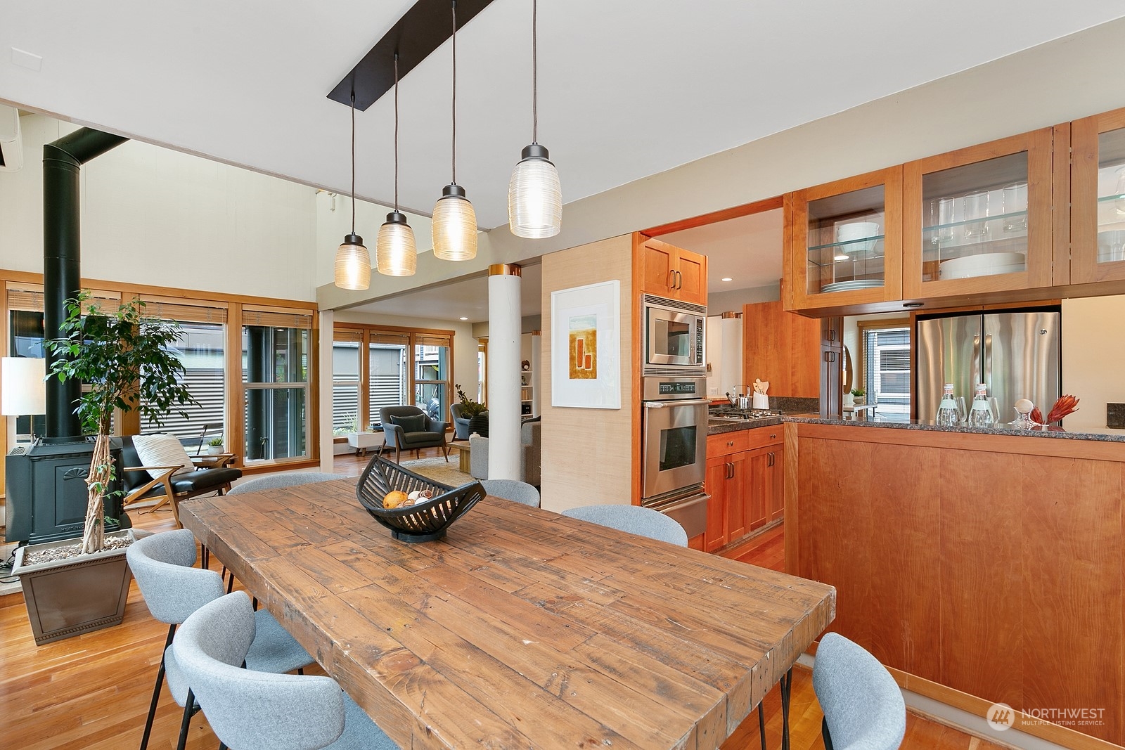 Open-plan kitchen and dining area with wood cabinets, stainless steel appliances, and a long rustic table.