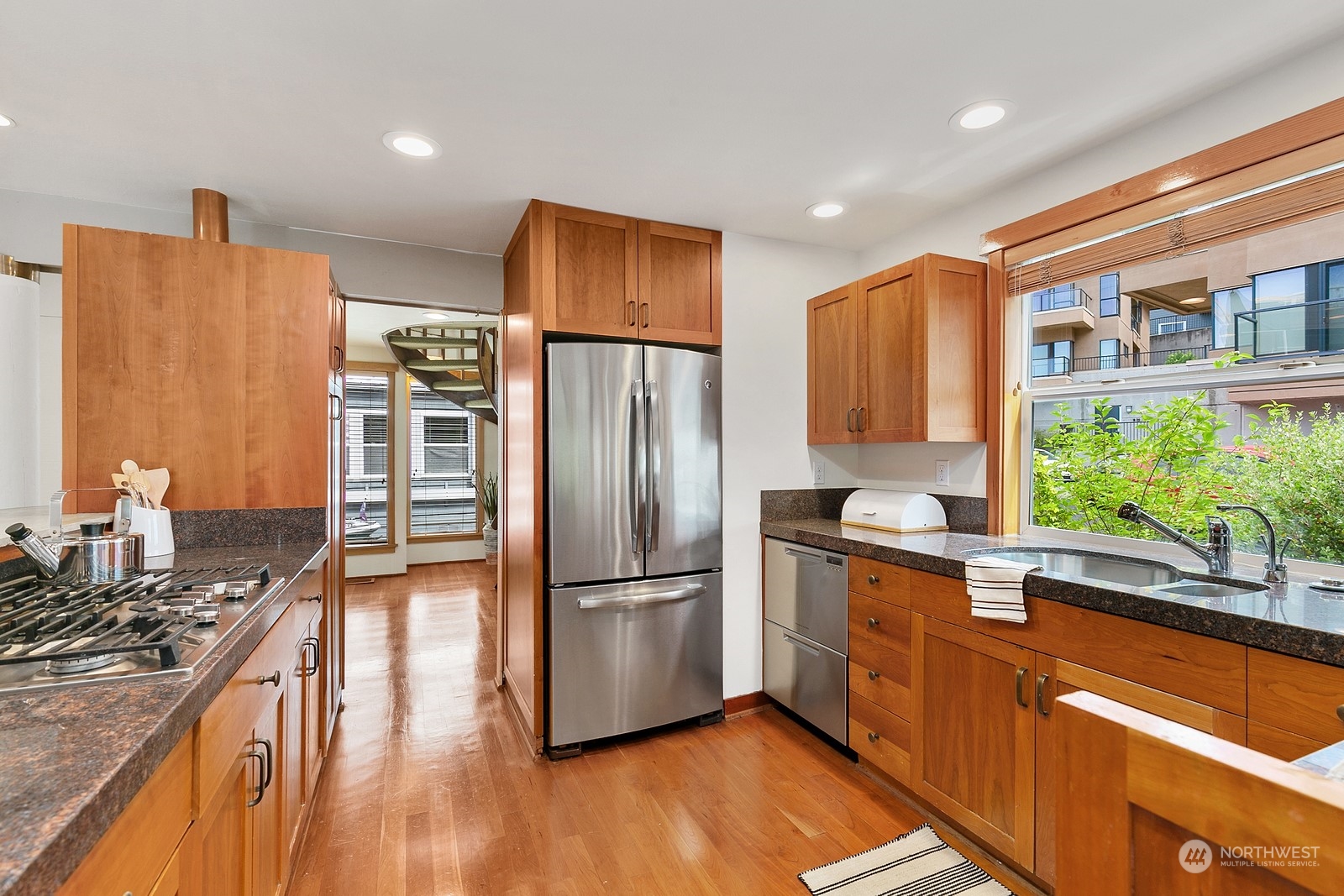 Kitchen with warm wood cabinets, granite counters, stainless appliances, and a window overlooking greenery.