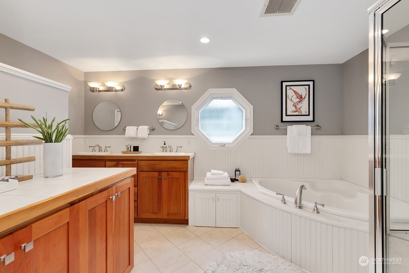 Bathroom with a wood double vanity, octagonal window, built-in soaking tub, and glass-enclosed shower.