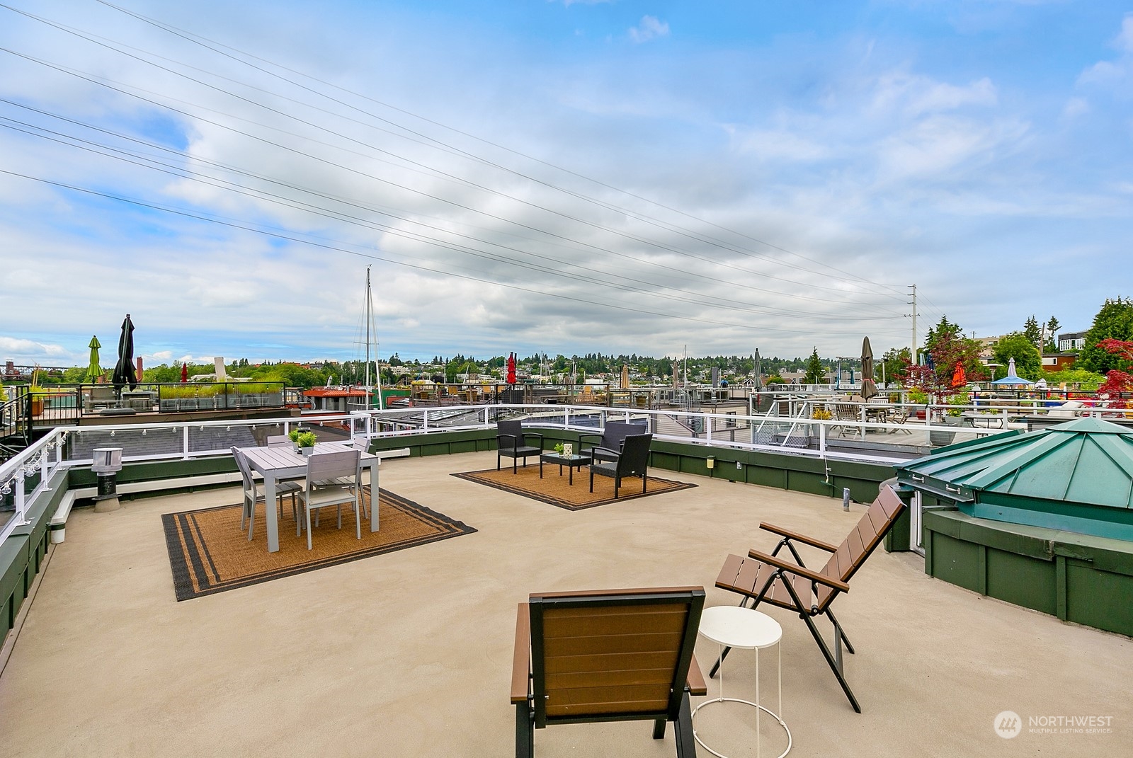 Rooftop terrace with outdoor dining and lounge seating overlooking a leafy neighborhood and sailboat masts.