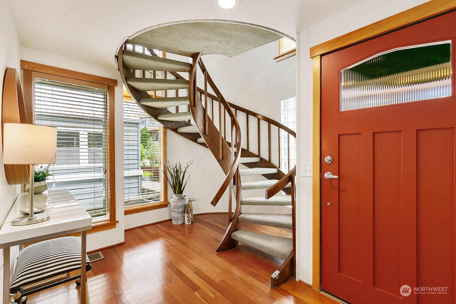 Entryway with a curved wooden staircase, red front door, hardwood floors, and large windows.