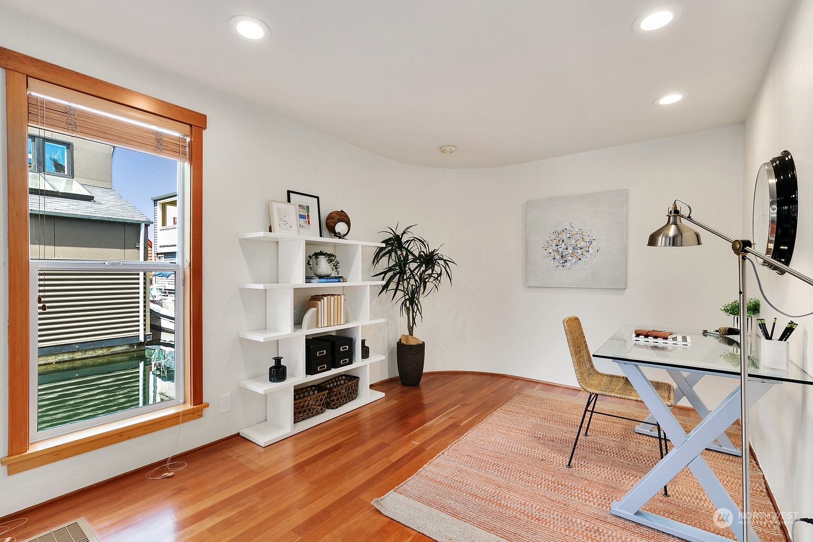 Staged home office with hardwood floors, a glass-top desk, and a window overlooking the water.