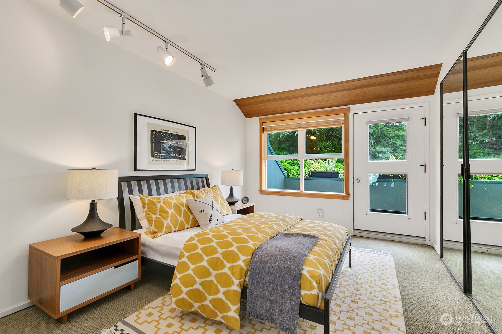 Bedroom with mustard patterned bedding, a wood-trimmed window, and mirrored closet doors.