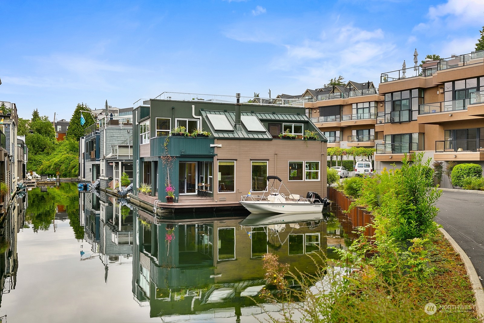 Floating home beside a small boat on a calm Seattle waterway, with rooftop terraces and neighboring residences.