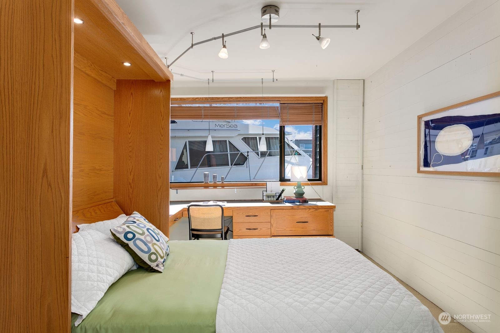 Bedroom with a built-in oak bed alcove and desk beneath a window overlooking a boat.