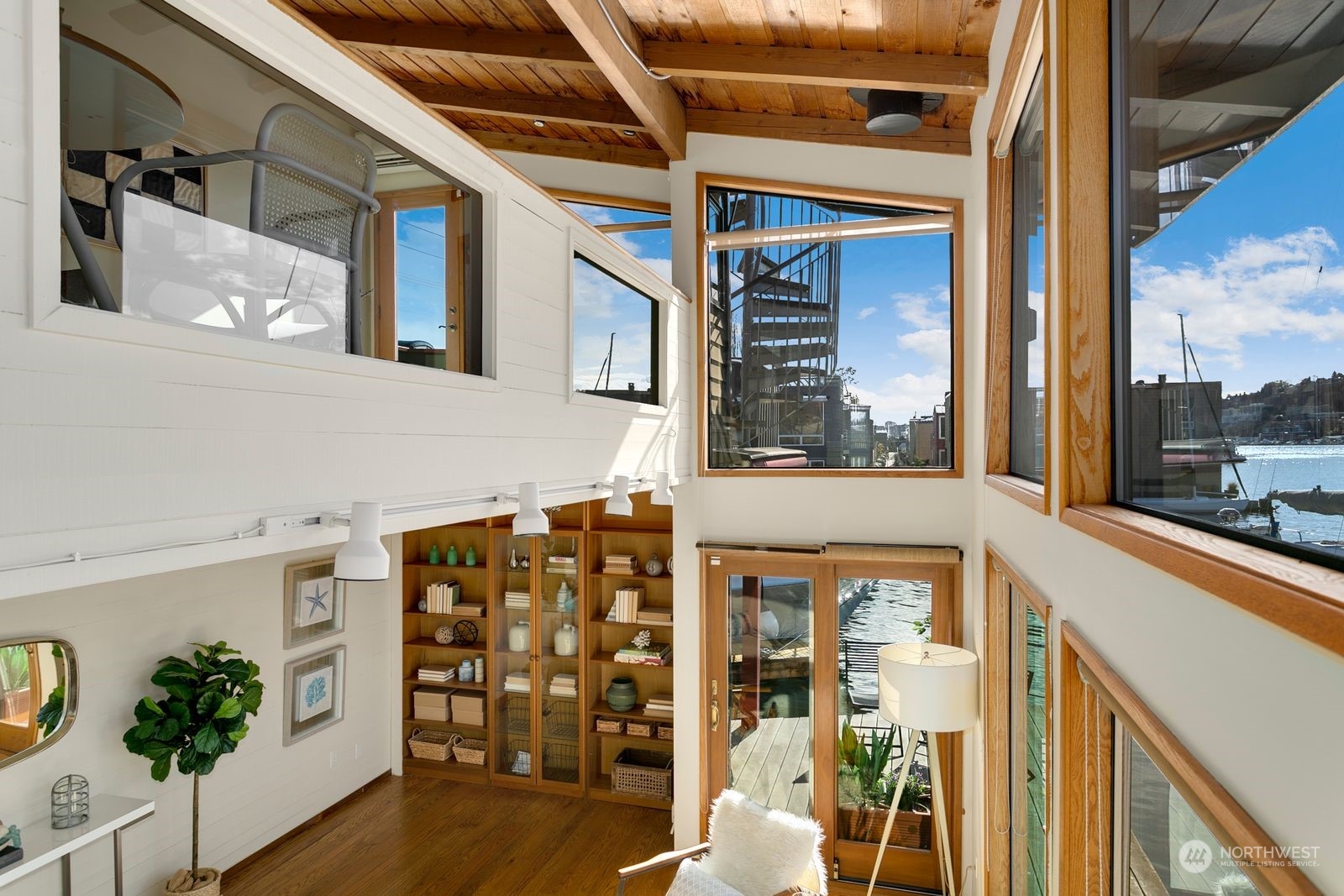 Waterfront living room with a vaulted wood ceiling, built-in shelves, and large windows overlooking the water.