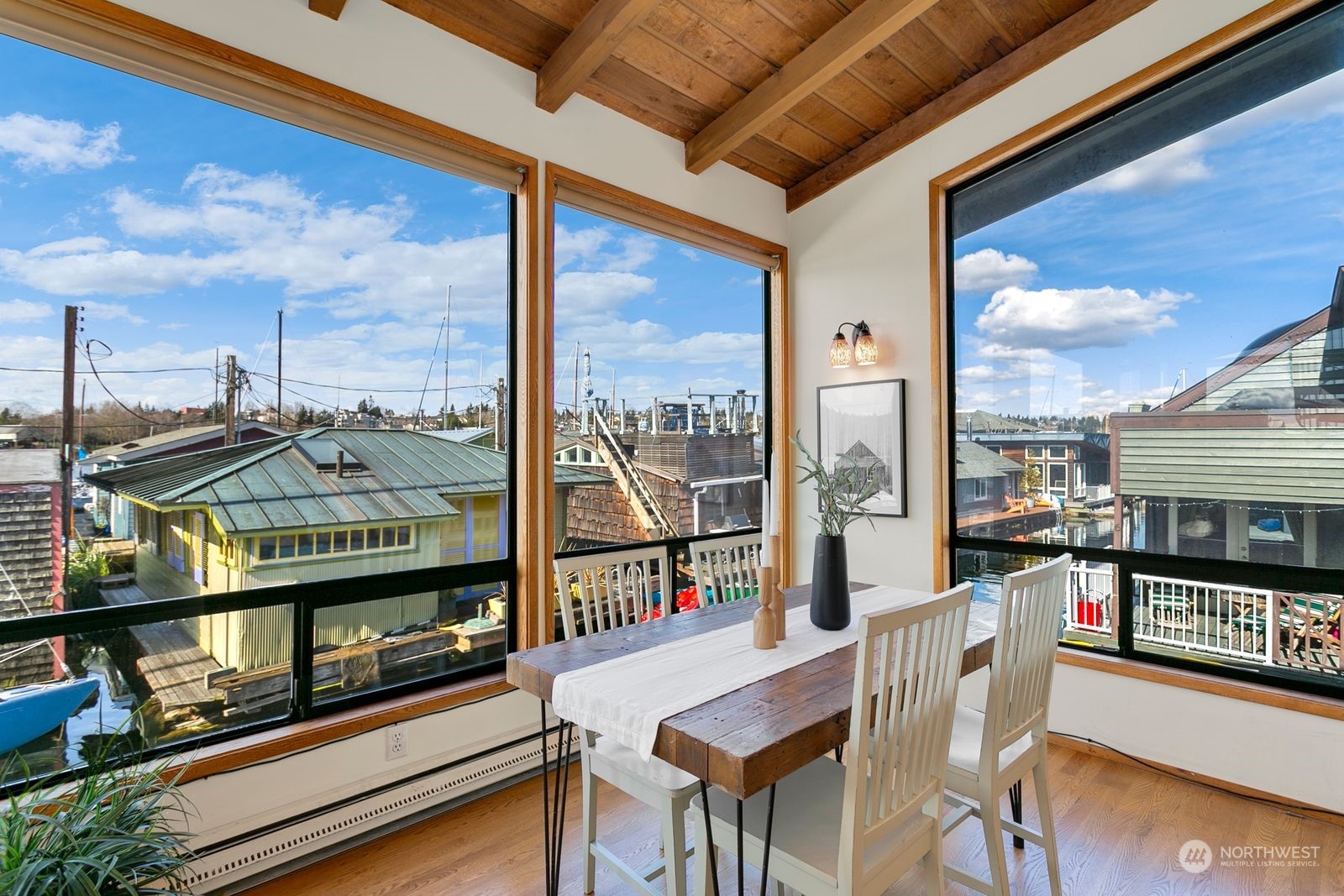 Dining area with exposed timber ceiling and large windows overlooking waterfront homes and docks.