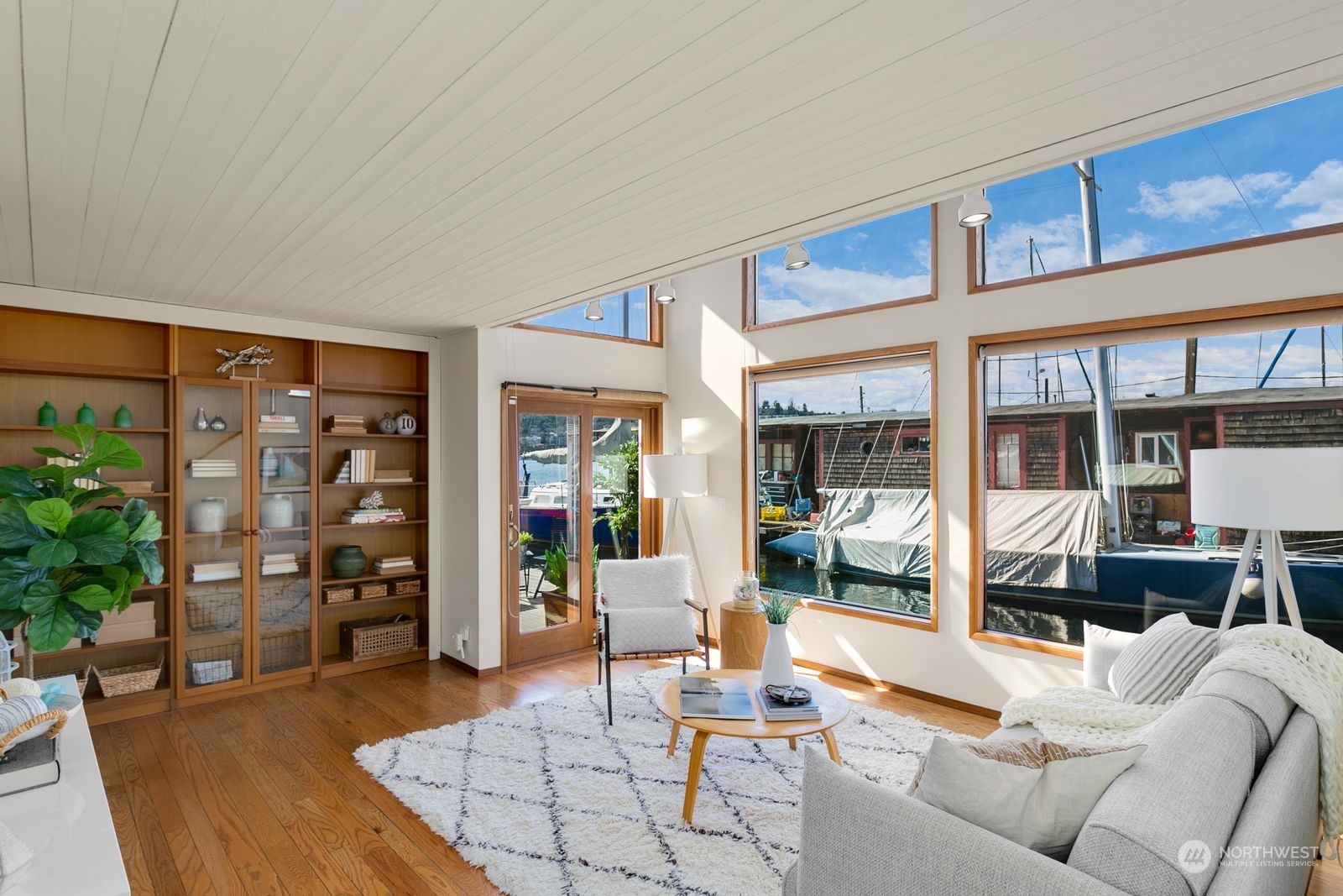 Living room with built-in wood shelving and large windows overlooking boats at a marina.