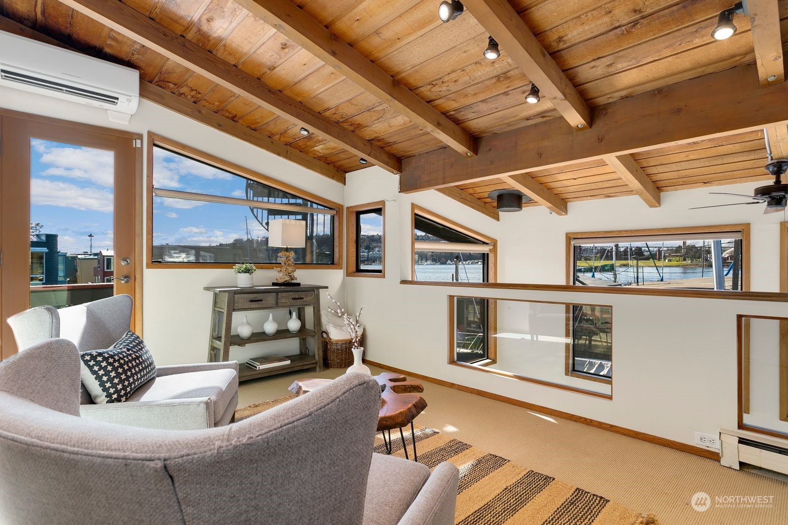 Living room with a vaulted wood ceiling, gray seating, and windows overlooking the water and boats.