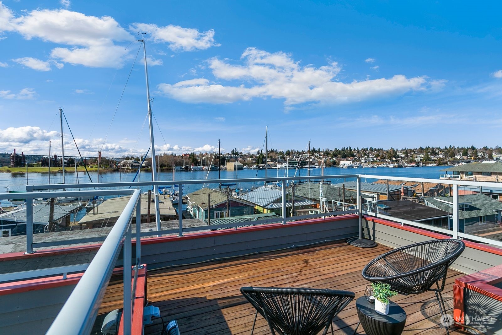 Rooftop deck overlooking Lake Union and a marina, with wood flooring and black woven chairs.