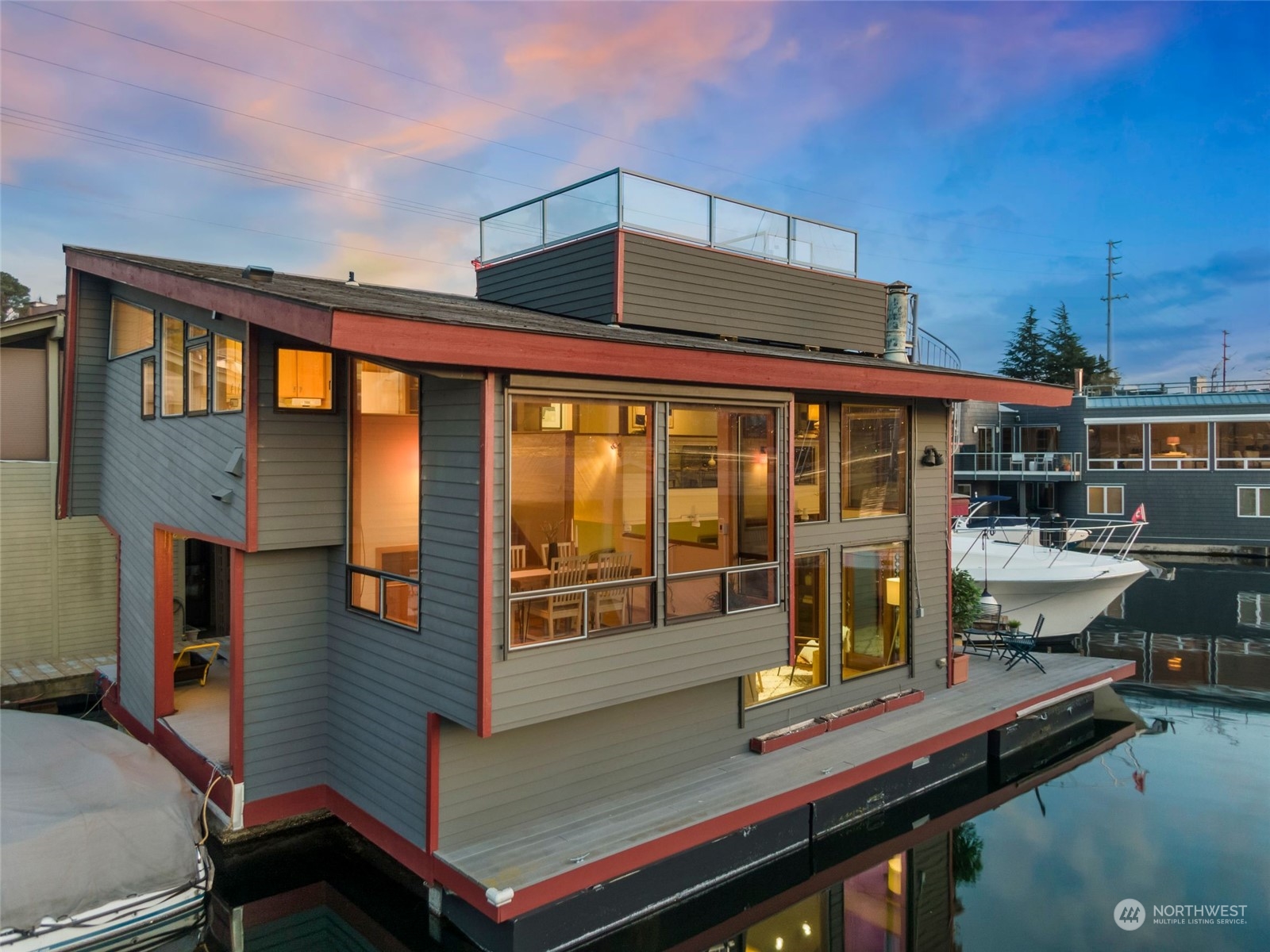Modern waterfront home with expansive windows, rooftop deck, and boat moored beside its dock.