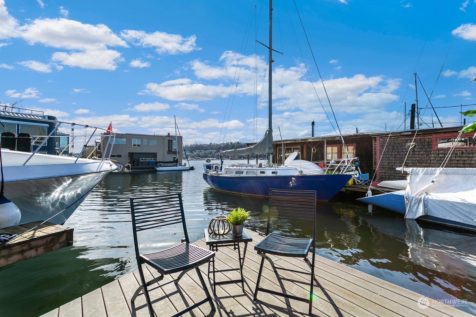 Waterfront deck with seating overlooking a marina and a prominent blue sailboat.