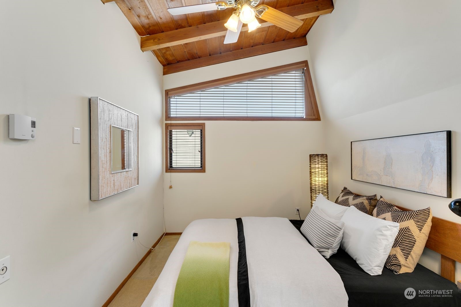 Bedroom with a vaulted wood ceiling, ceiling fan, high windows, and a neatly made bed.