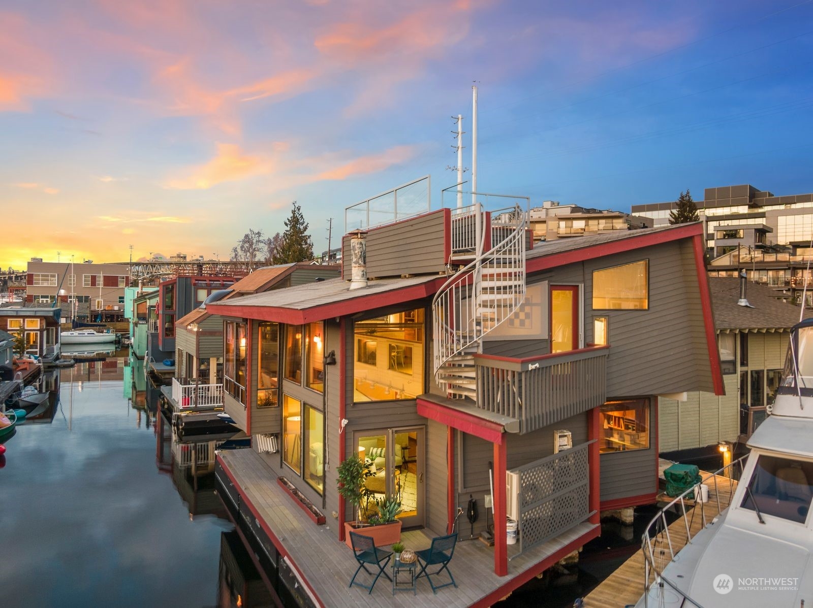 Waterfront houseboat with a spiral staircase and deck overlooking the marina at sunset.