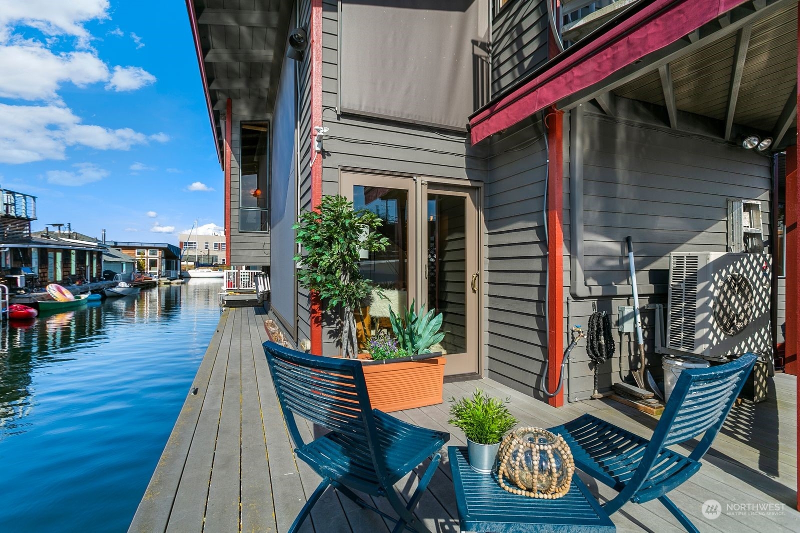 Waterfront home deck with blue patio chairs, potted plants, and views across the canal.