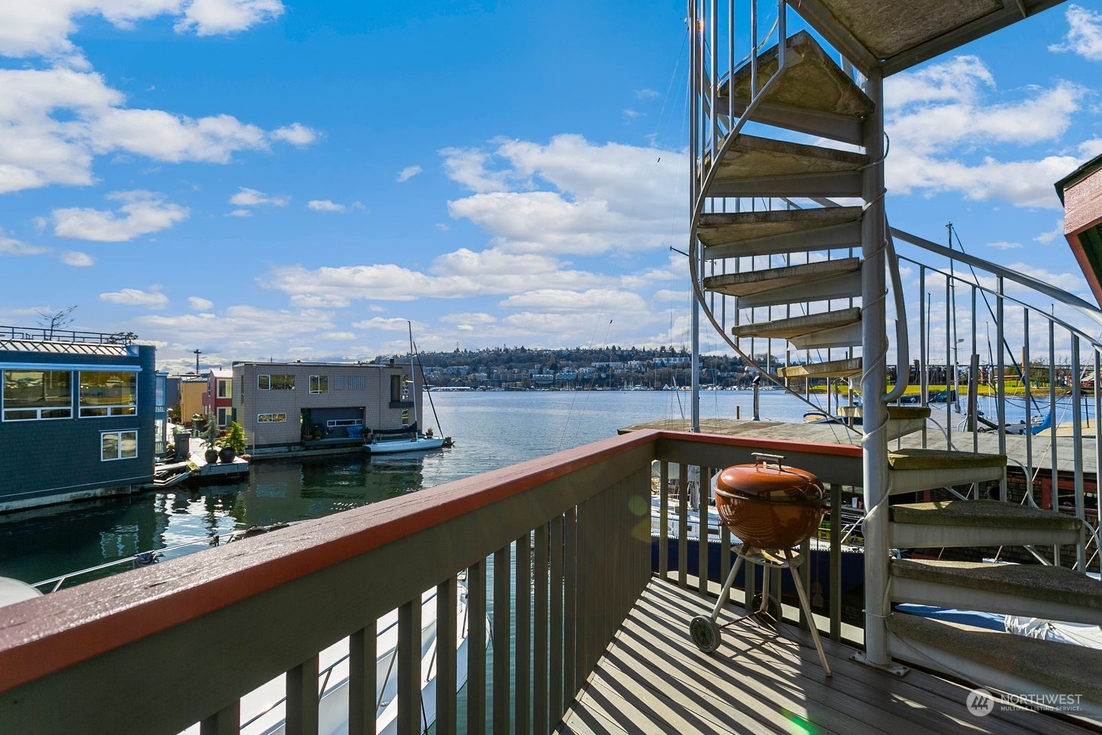 Waterfront deck with a spiral staircase and barbecue overlooking a marina and boats.