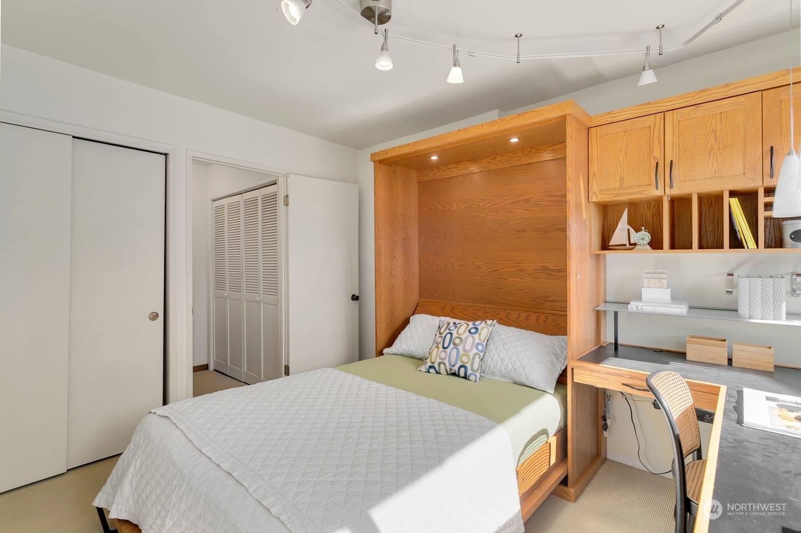 Bedroom with a wood built-in bed, overhead cabinets, open shelving, and a desk.