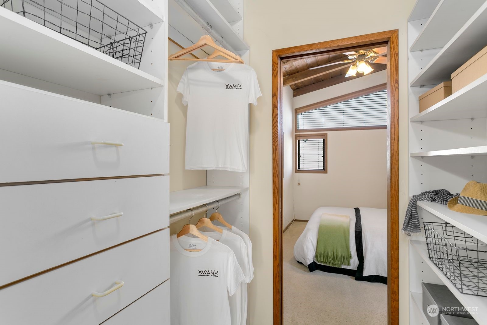 Walk-in closet with white built-ins and a wood-trimmed doorway to a bedroom.
