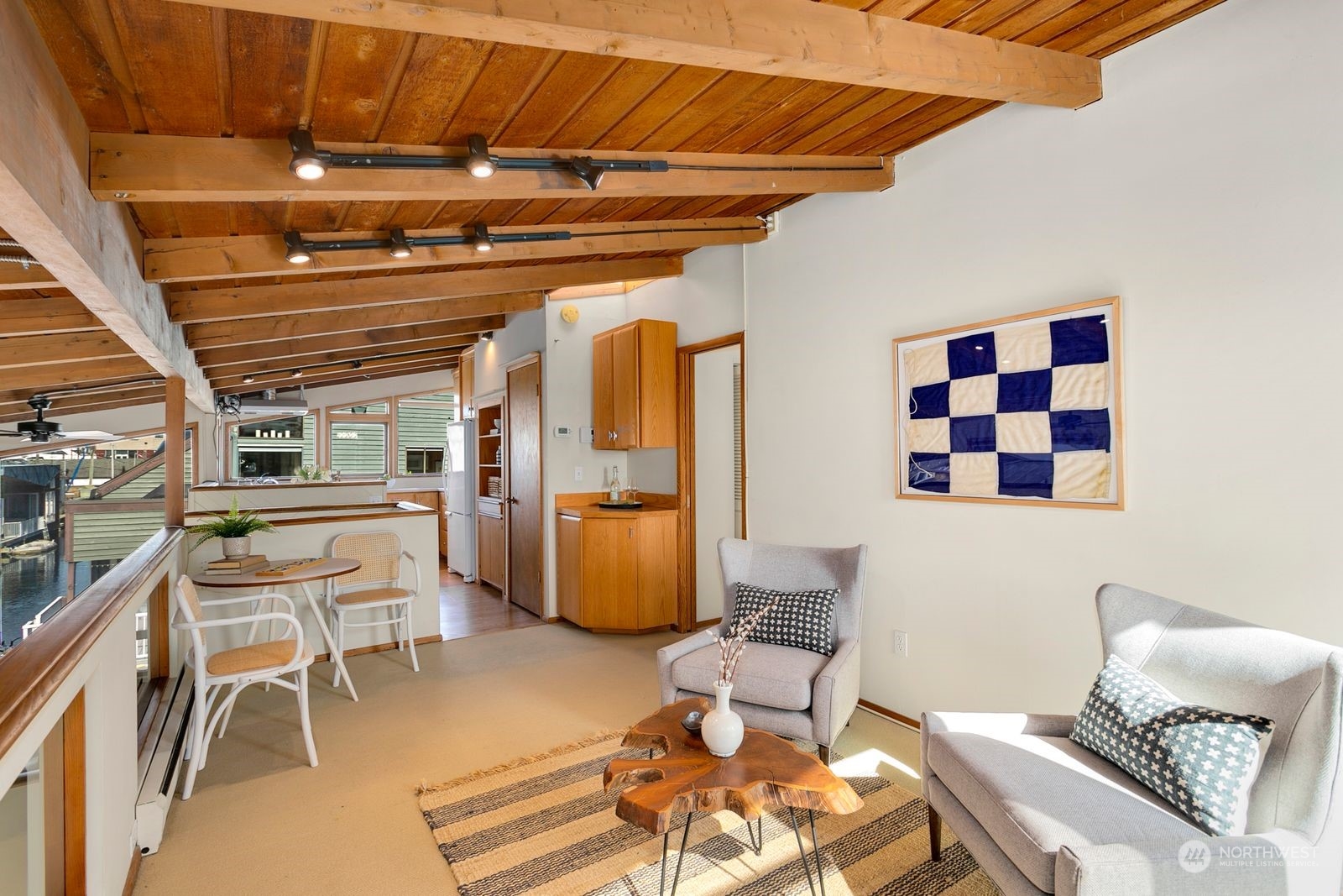 Open-plan living area with exposed wood beams, gray armchairs, and a waterfront view.