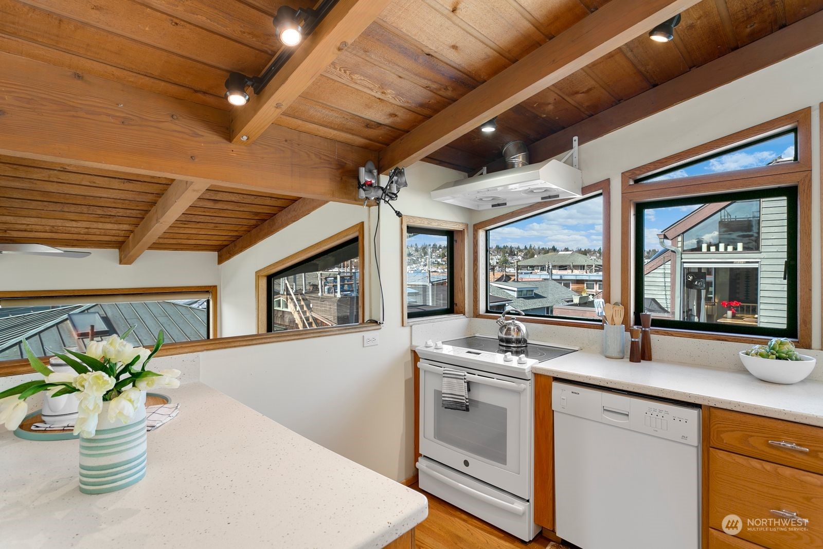 Kitchen with white counters, exposed wood ceiling beams, and large windows overlooking nearby rooftops.