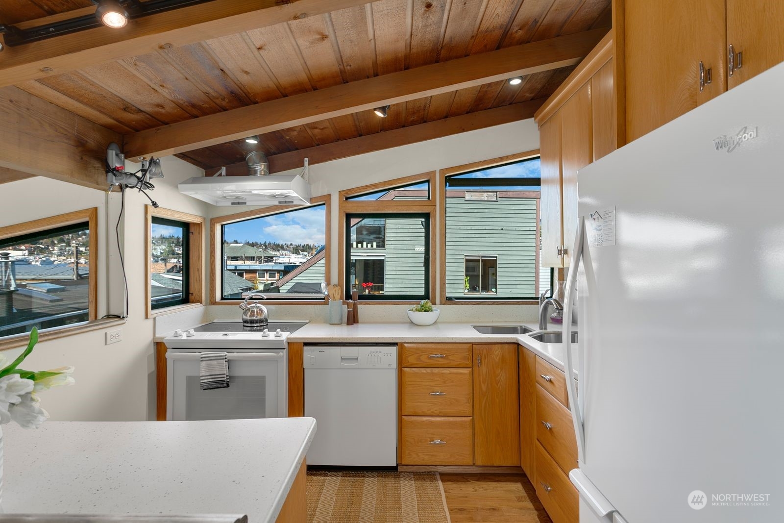 Kitchen with a vaulted wood ceiling, warm cabinetry, and large windows overlooking rooftops and water.