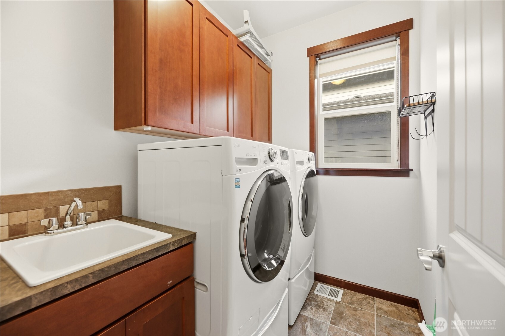 Laundry room with front-loading washer and dryer, wood cabinets, and a utility sink.
