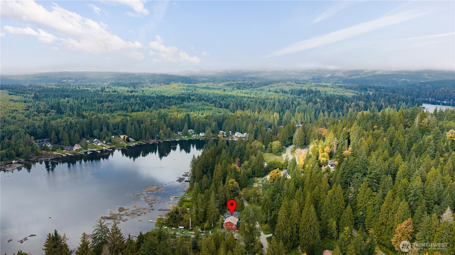 Aerial view of a red house beside a wooded lake shoreline, marked with a red location pin.