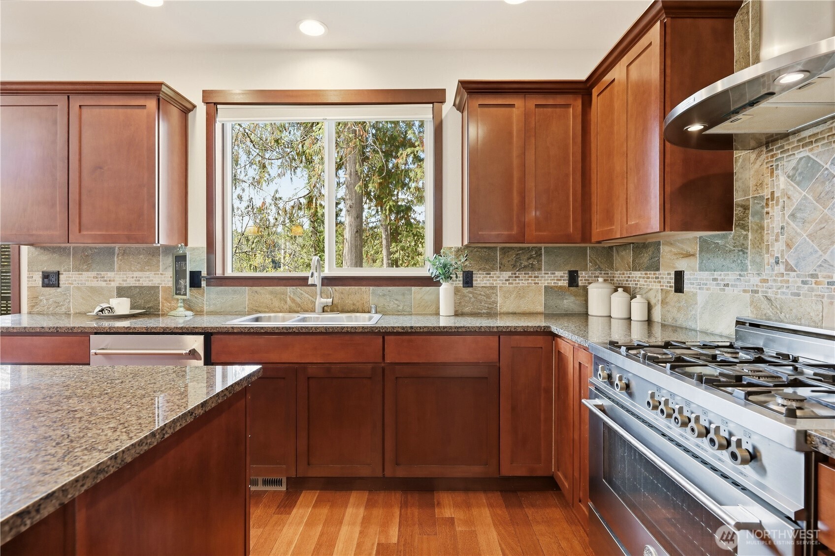 Kitchen with rich wood cabinets, stone backsplash, granite counters, and a stainless-steel gas range.